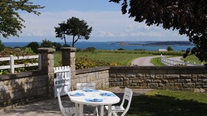 Eine Terrasse im Freien mit einem weißen Tisch und Stühlen, Steinmauern und Blick aufs Meer.