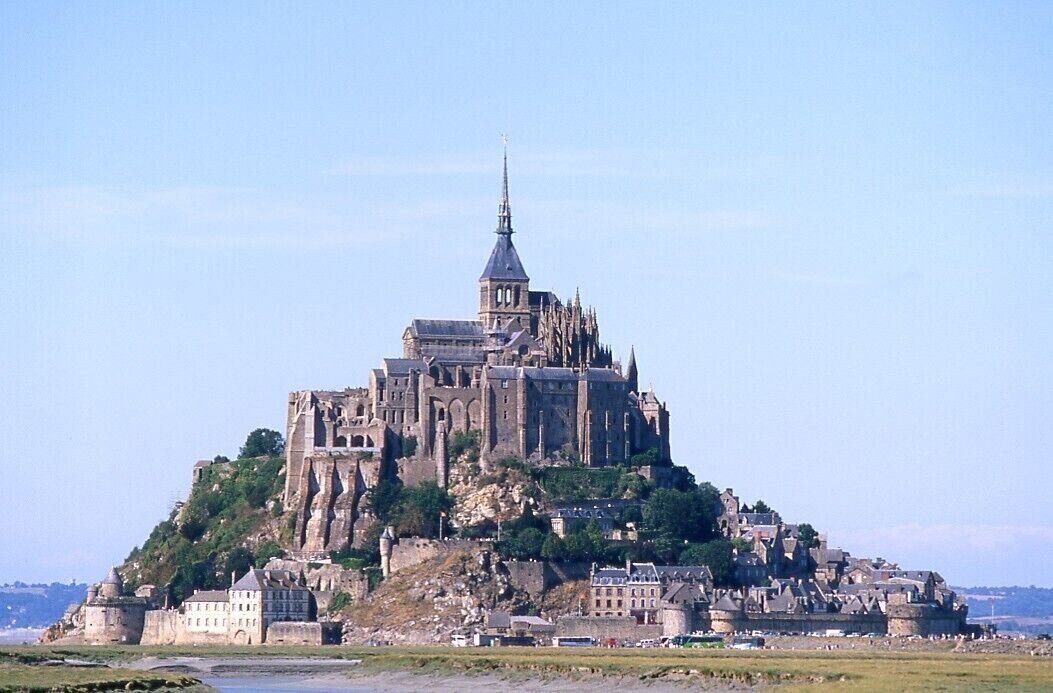 A large historic castle with multiple towers and a prominent spire, situated on a hill with surrounding buildings.