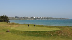 Ein Golfplatz mit Blick auf das Meer und eine entfernte Küstenlinie mit Gebäuden.