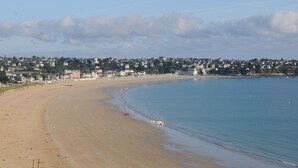 Ein weiter Sandstrand mit ruhiger See, ein kleines Boot und eine in der Ferne liegende Stadt mit Gebäuden.