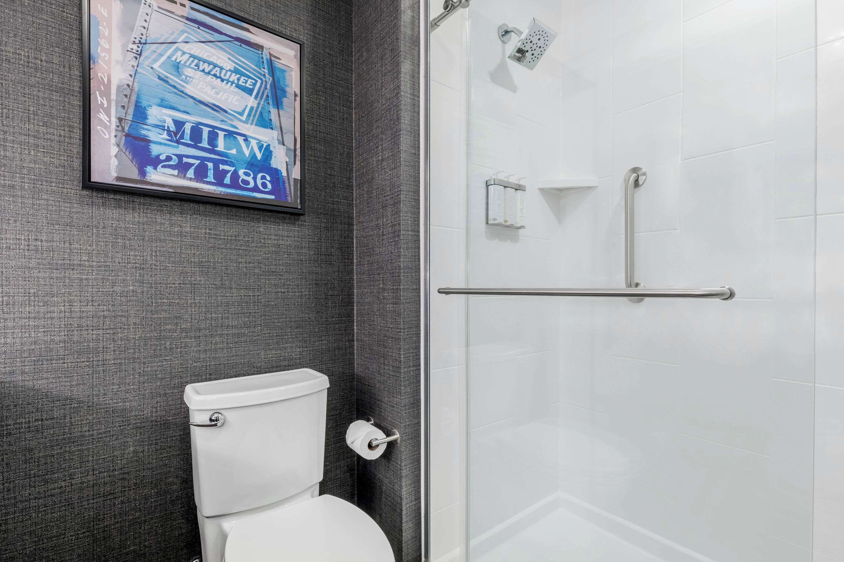 A bathroom with a toilet, a glass shower enclosure, and a framed sign on the wall.