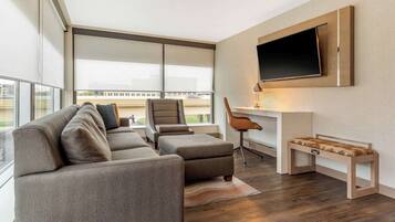 Una sala moderna con sofá, reposapiés y un banco, un escritorio con silla, y un televisor montado.
