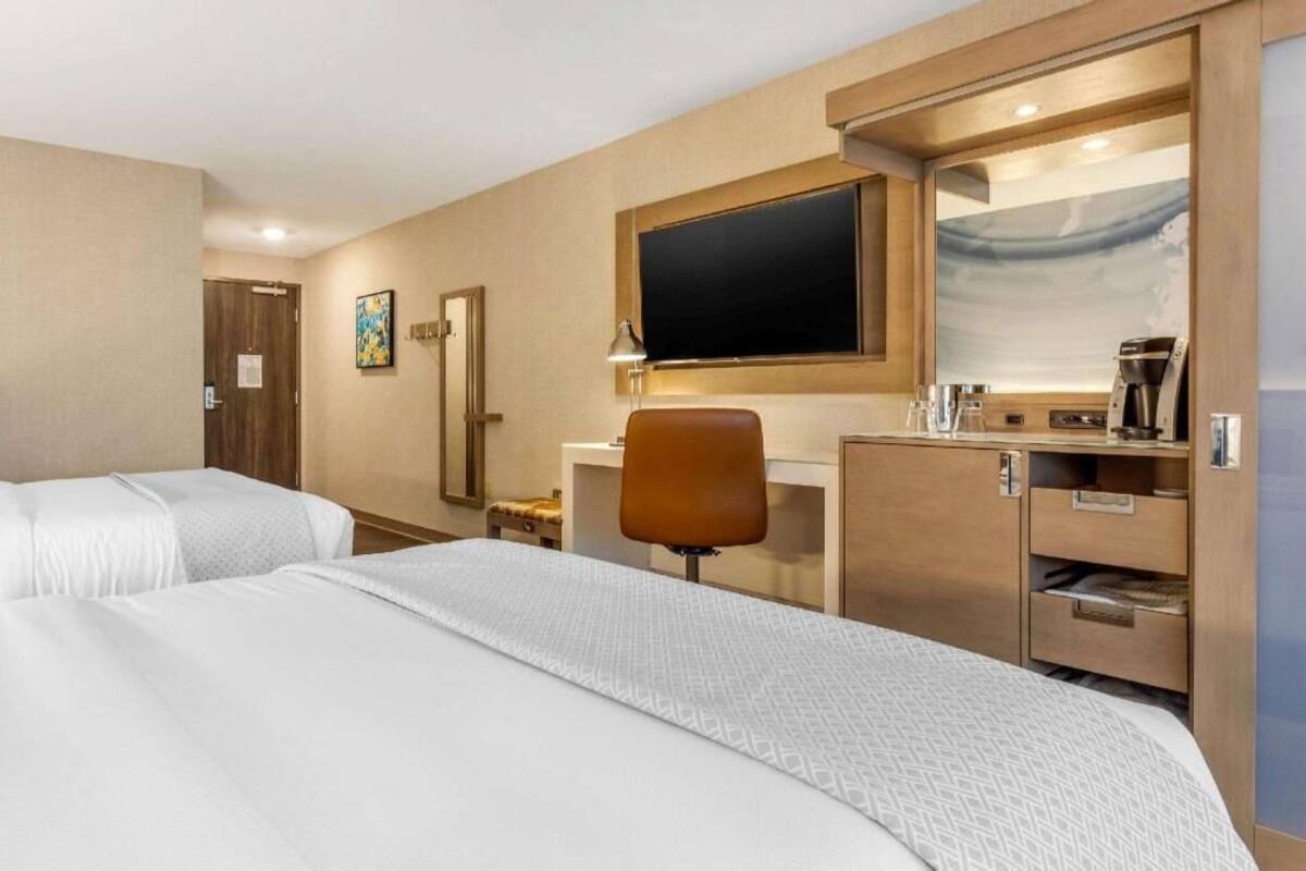 Hotellihuone, jossa on kaksi sänkyä, työpöytä, tuoli, televisio ja kahvinkeitin.