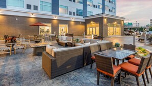 A modern outdoor patio with wicker furniture, a barbecue grill, and a view of a multi-story building. - Cambria Hotel Milwaukee Downtown (Milwaukee)