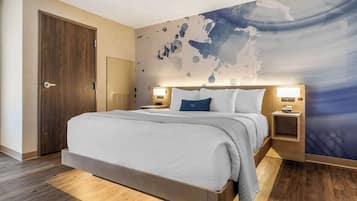 A modern hotel room with a large bed, wooden flooring, a world map mural, and two bedside tables with lamps.