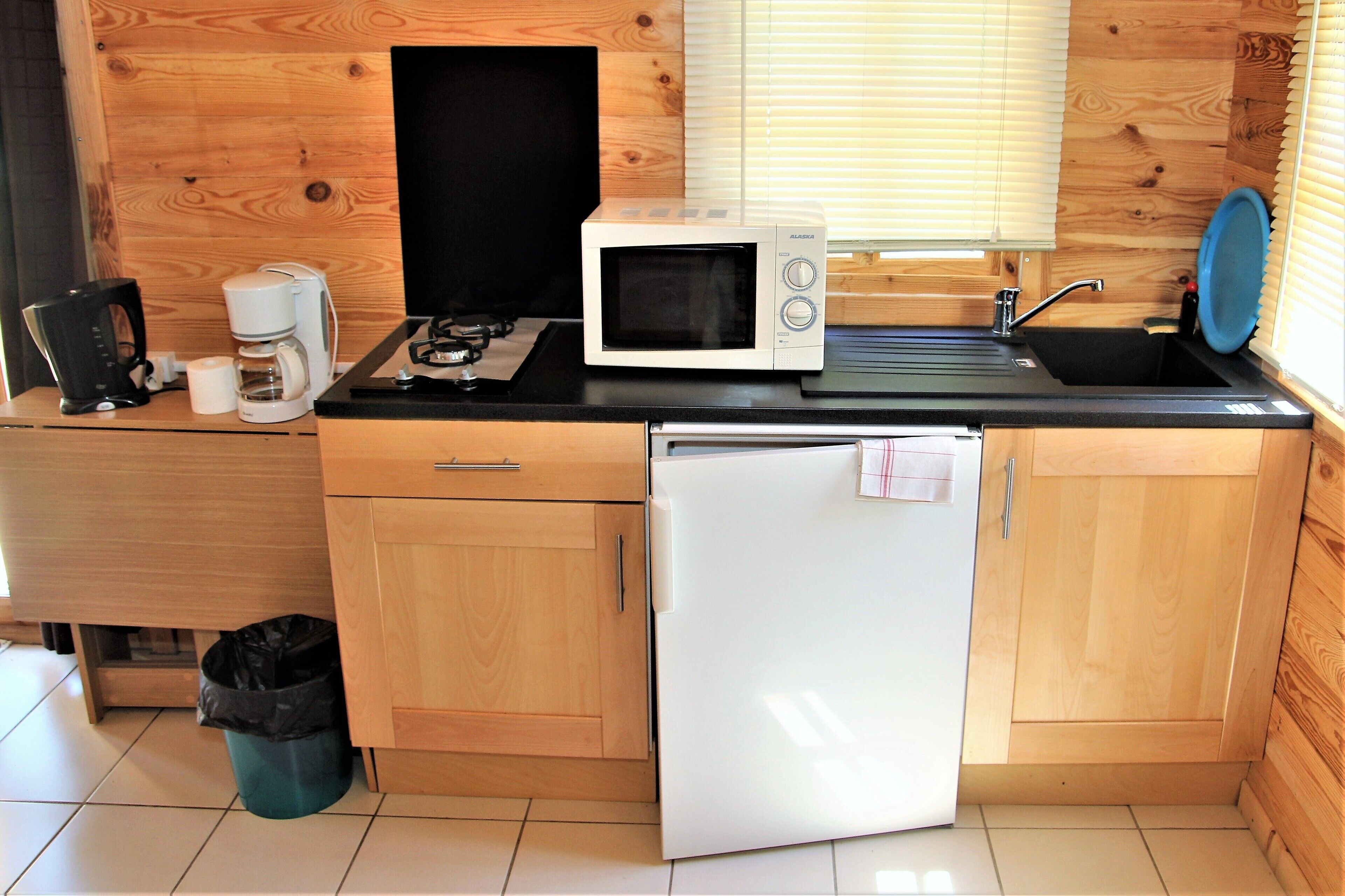 A compact kitchen with a microwave, coffee maker, sink, and a refrigerator.