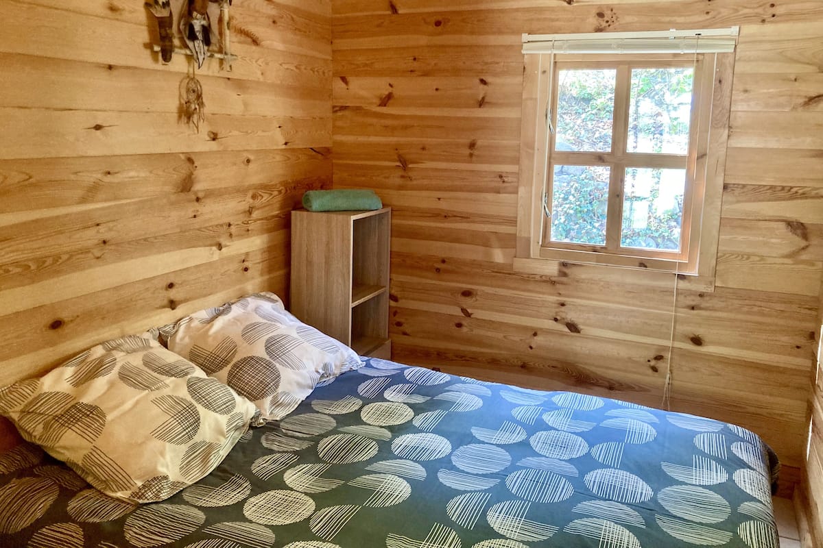 Ein Zimmer in einer Holzhütte mit einem Bett, einem Fenster und einem Regal.