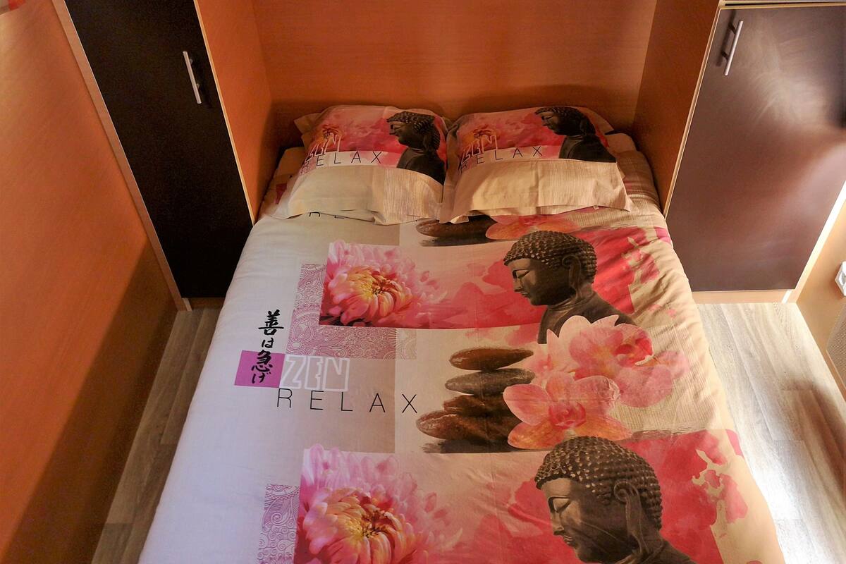 Ein Bett mit Zen-Relax-Ambiente, inklusive Buddha-Statue und rosa Blüten.