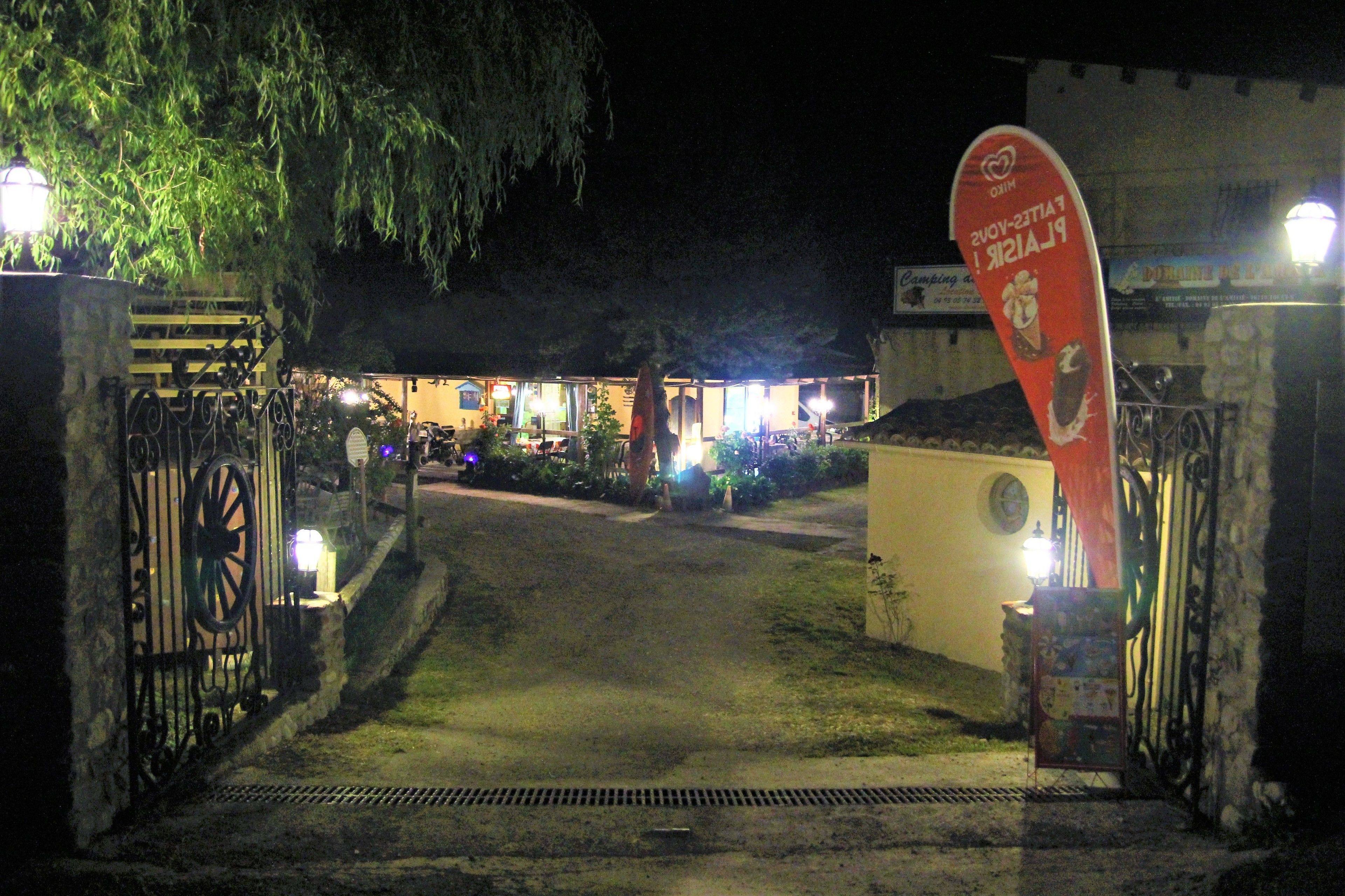 A gated entrance to a building at night with illuminated signs and a pathway leading to the entrance.