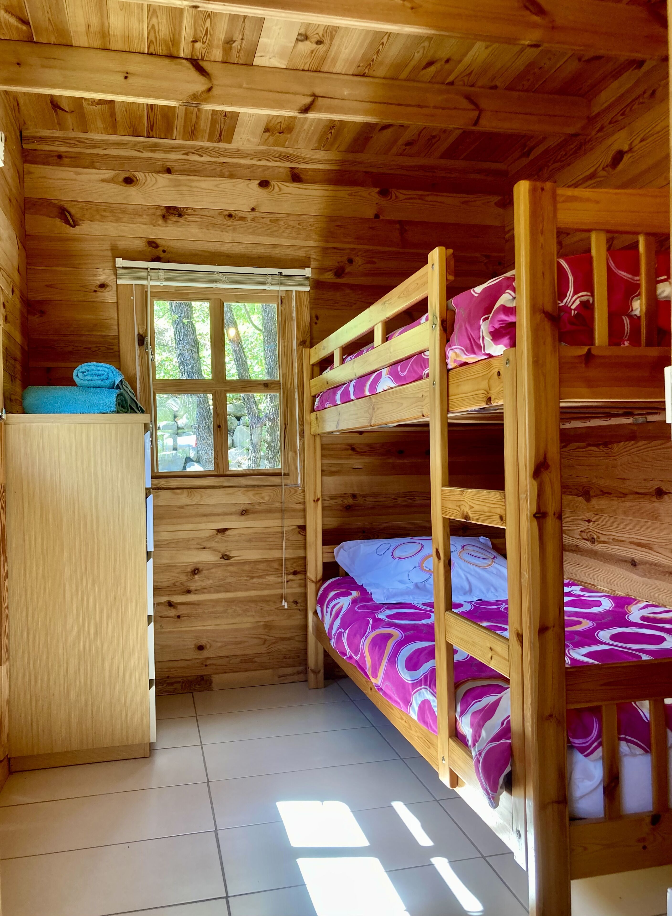 Una habitación tipo cabaña de madera con literas, una ventana y un pequeño armario de madera.