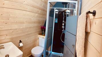 Een badkamer met houten lambrisering, een glazen douchecabine, toilet en wastafel.