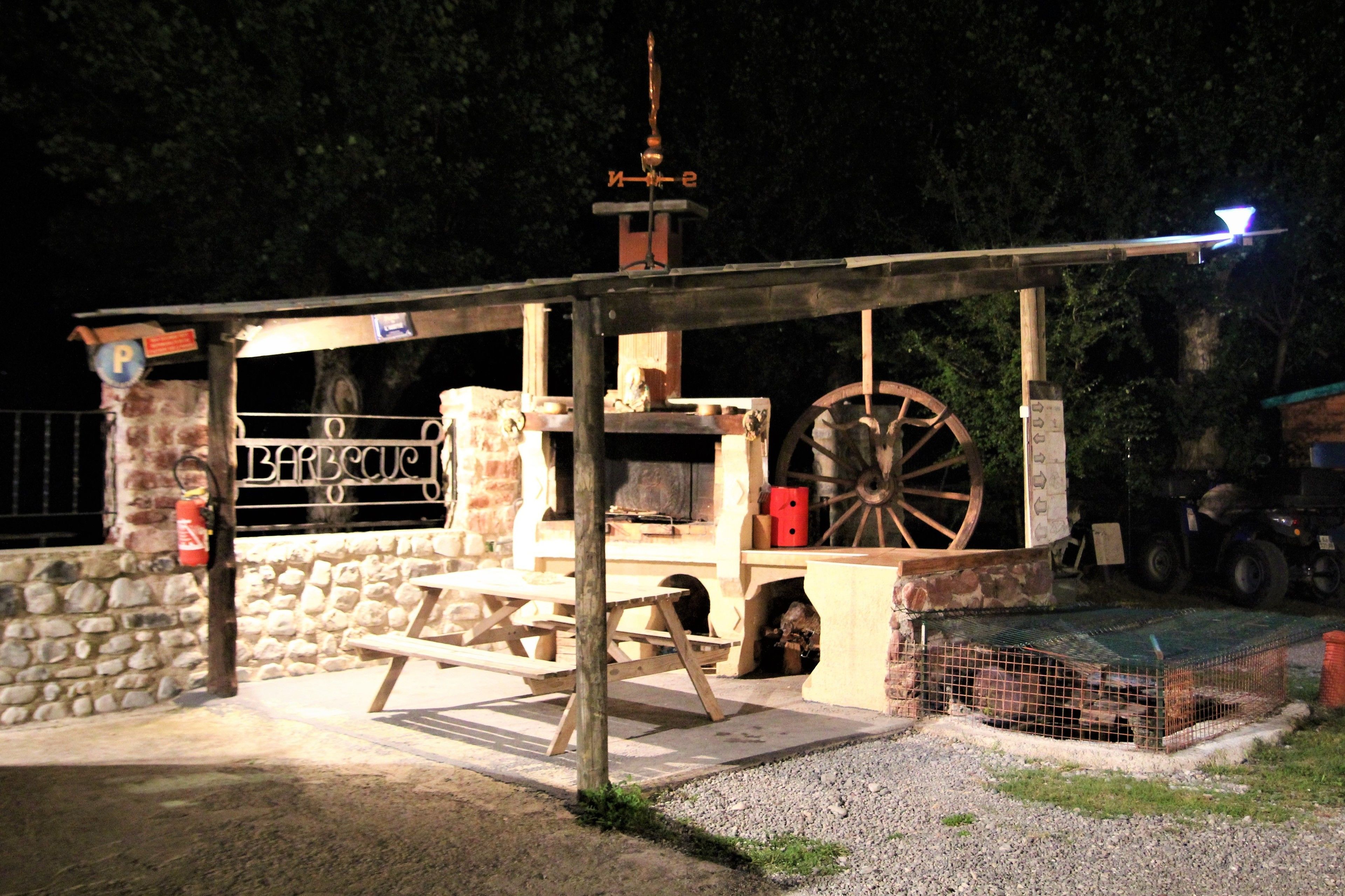 Ein rustikaler Essbereich im Freien mit einer Steinwand, Holztischen und einem großen Holzwagen.