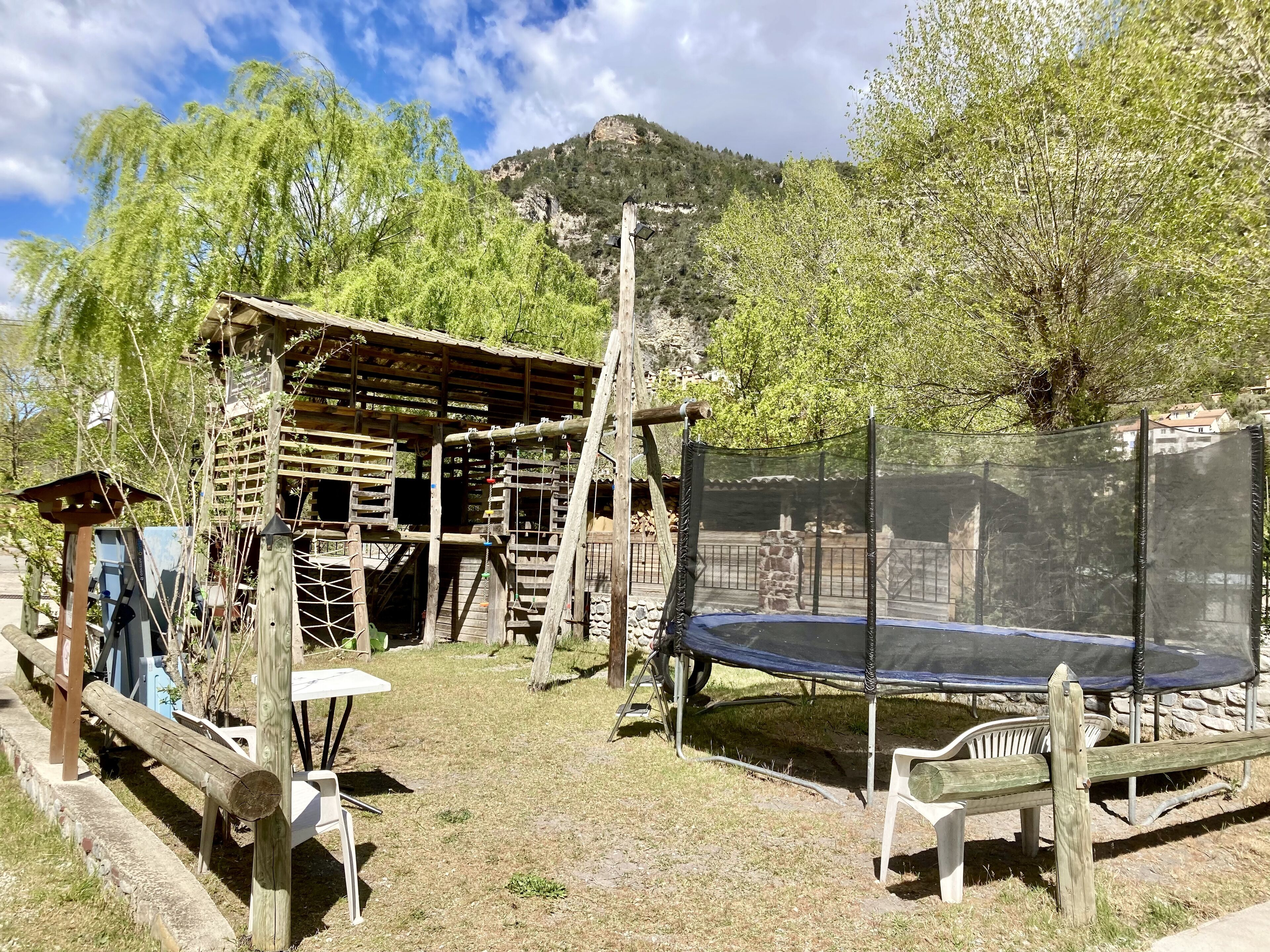 A wooden play structure with a trampoline and a covered seating area.