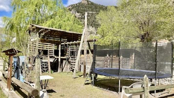 A wooden play structure with a trampoline and a covered seating area.