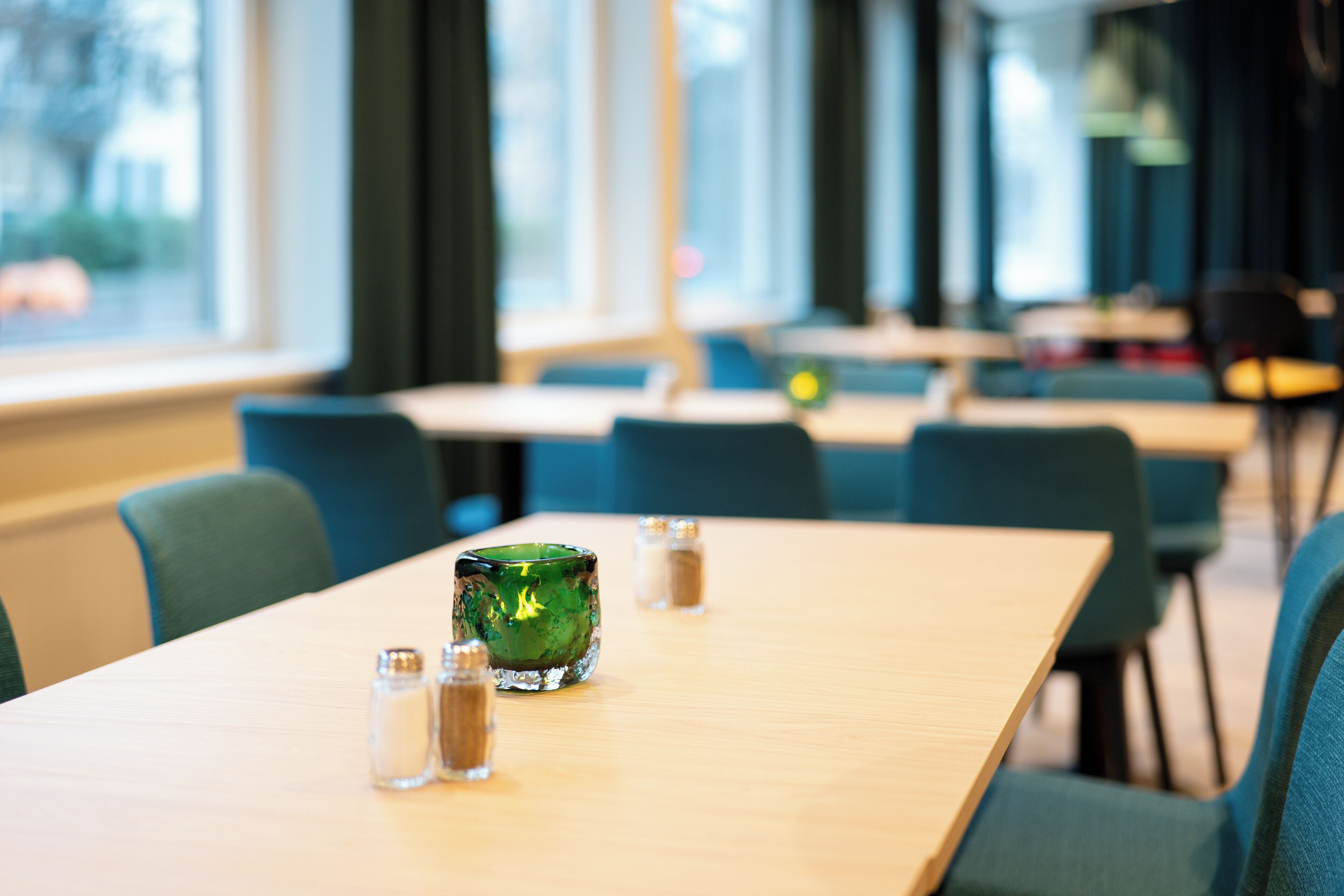 A dining area with tables and chairs, salt and pepper shakers, and a green glass container.