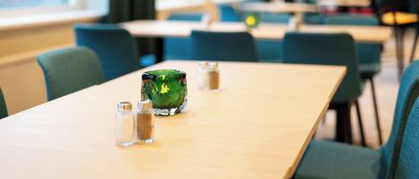 A dining area with tables and chairs, salt and pepper shakers, and a green glass container.