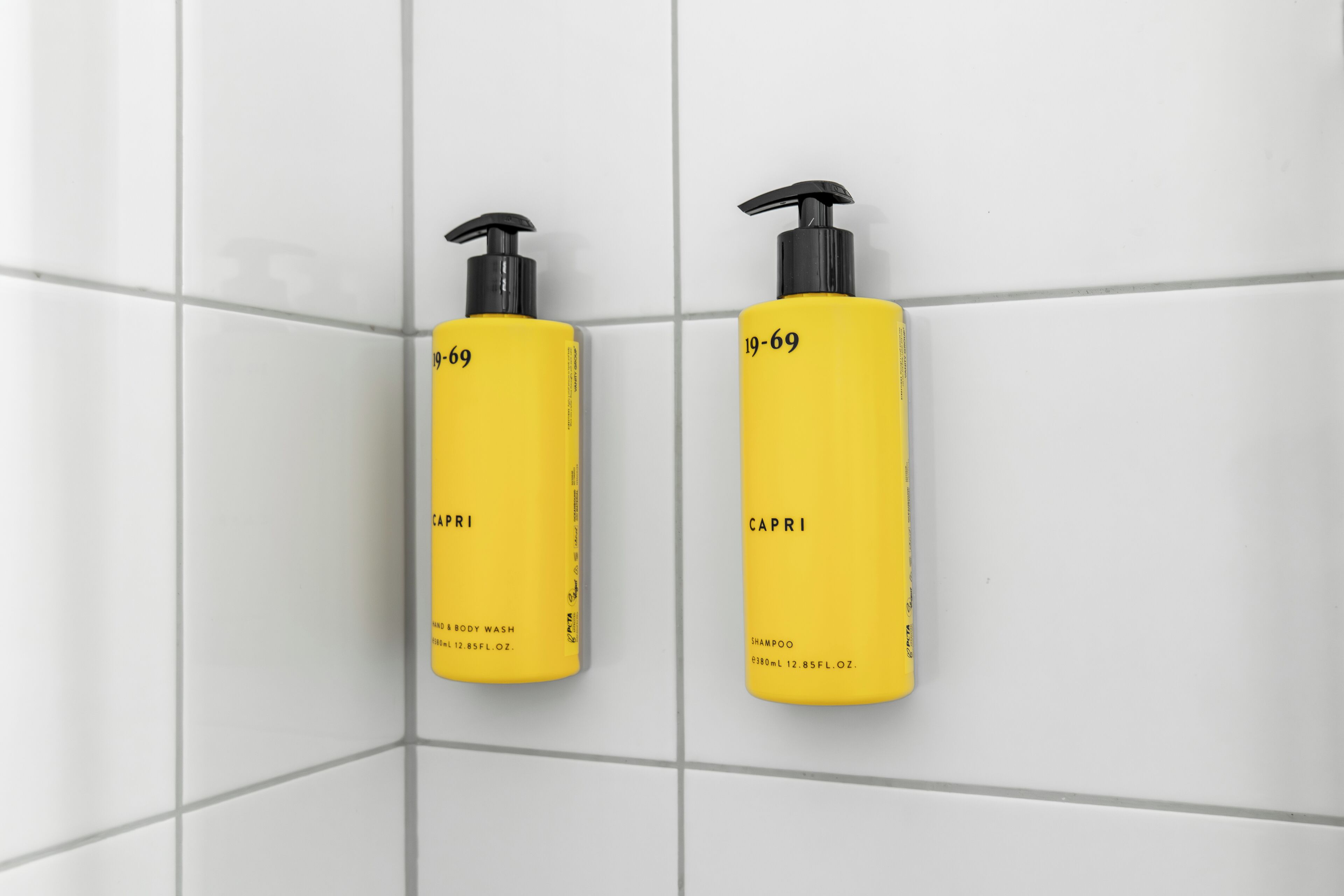 Two yellow bottles labeled "LAPI" and "CAPRI" on a white tiled wall.