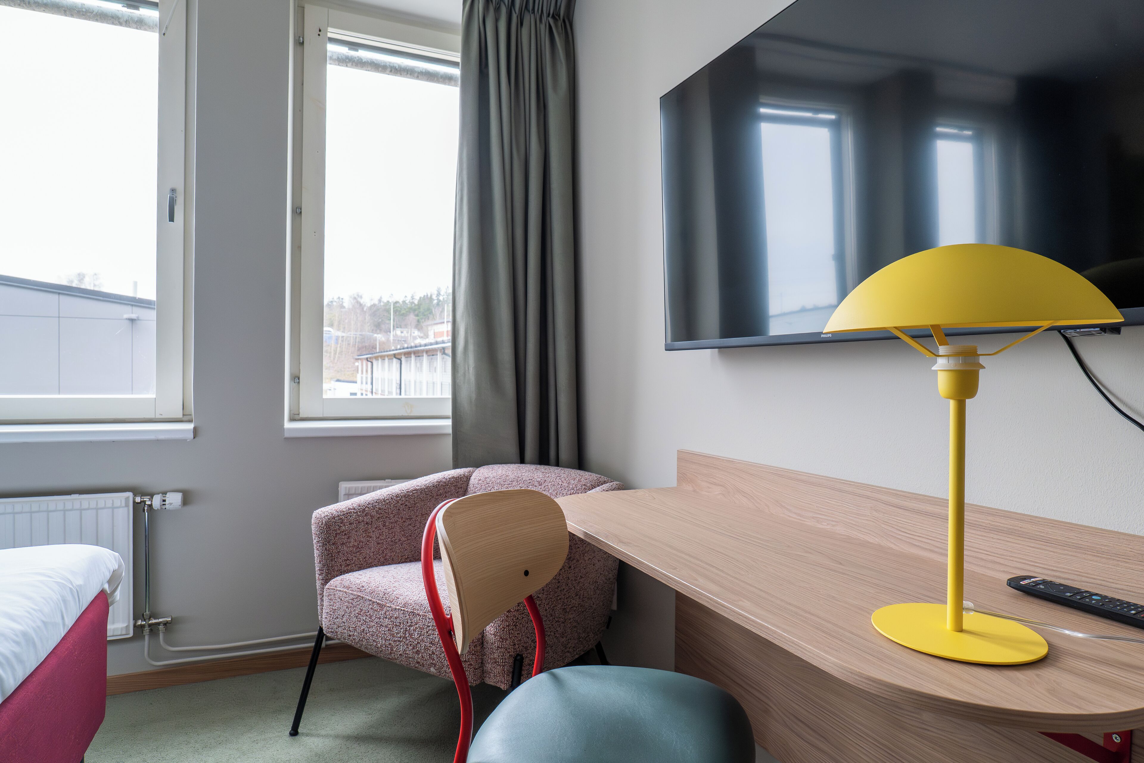 A hotel room with a bed, a desk, a chair, a TV, and a window with curtains.