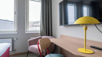A hotel room with a bed, a desk, a chair, a TV, and a window with curtains.