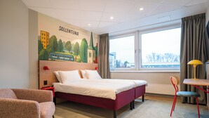 A hotel room with a bed, a chair, a table, a window, and a mural on the wall. - Good Morning Sollentuna (Sollentuna)
