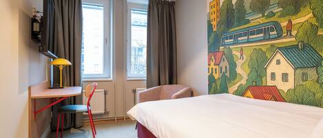 A hotel room with a bed, a desk with a chair, a TV, and a window with curtains.