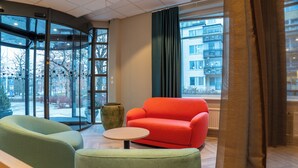 A modern lobby with a glass revolving door, a red sofa, and green armchairs. - Good Morning Sollentuna (Sollentuna)