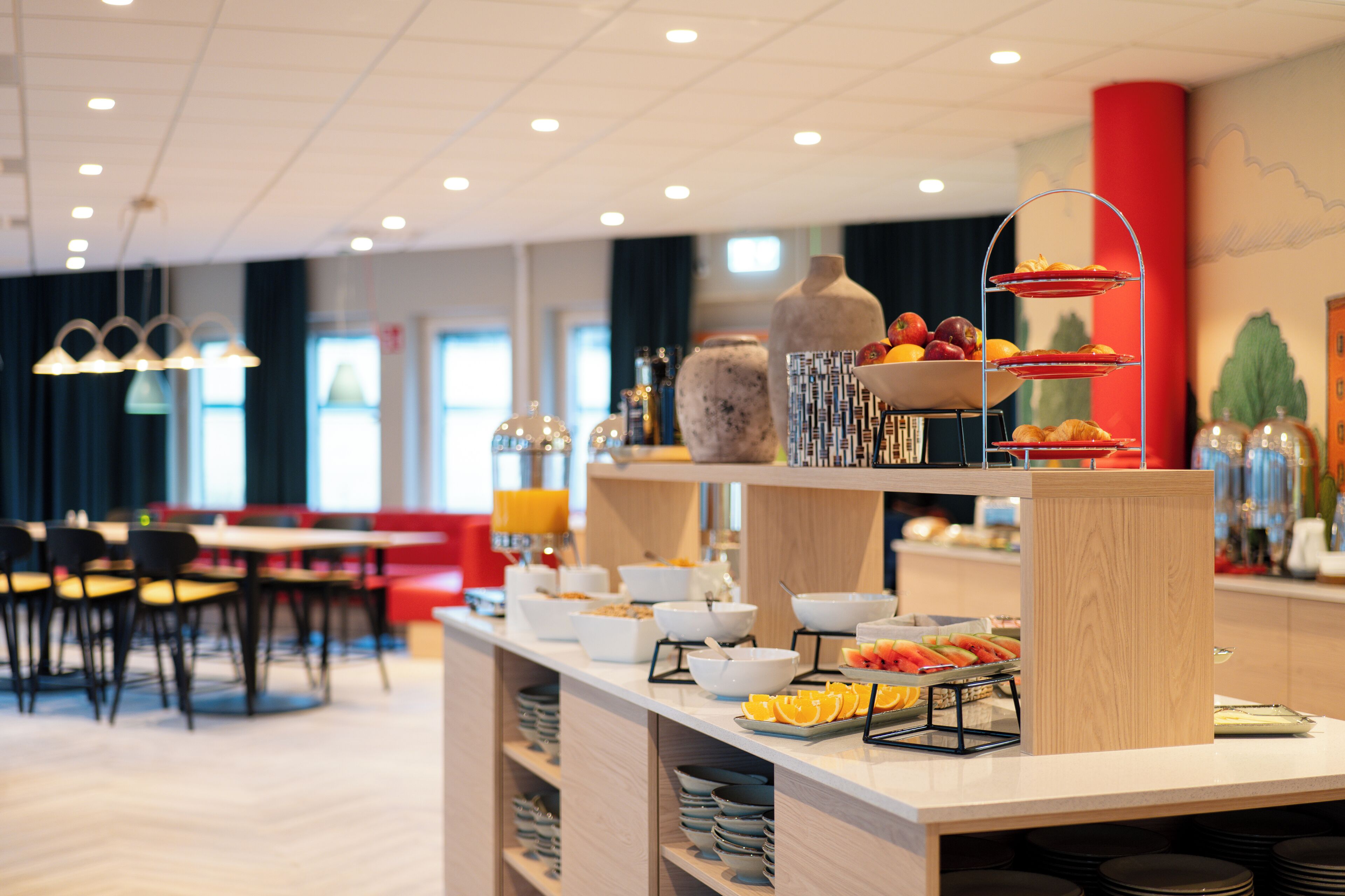 Un espace buffet avec divers plats et des plats de service disposés sur un comptoir, avec des sièges et des tables en arrière-plan.