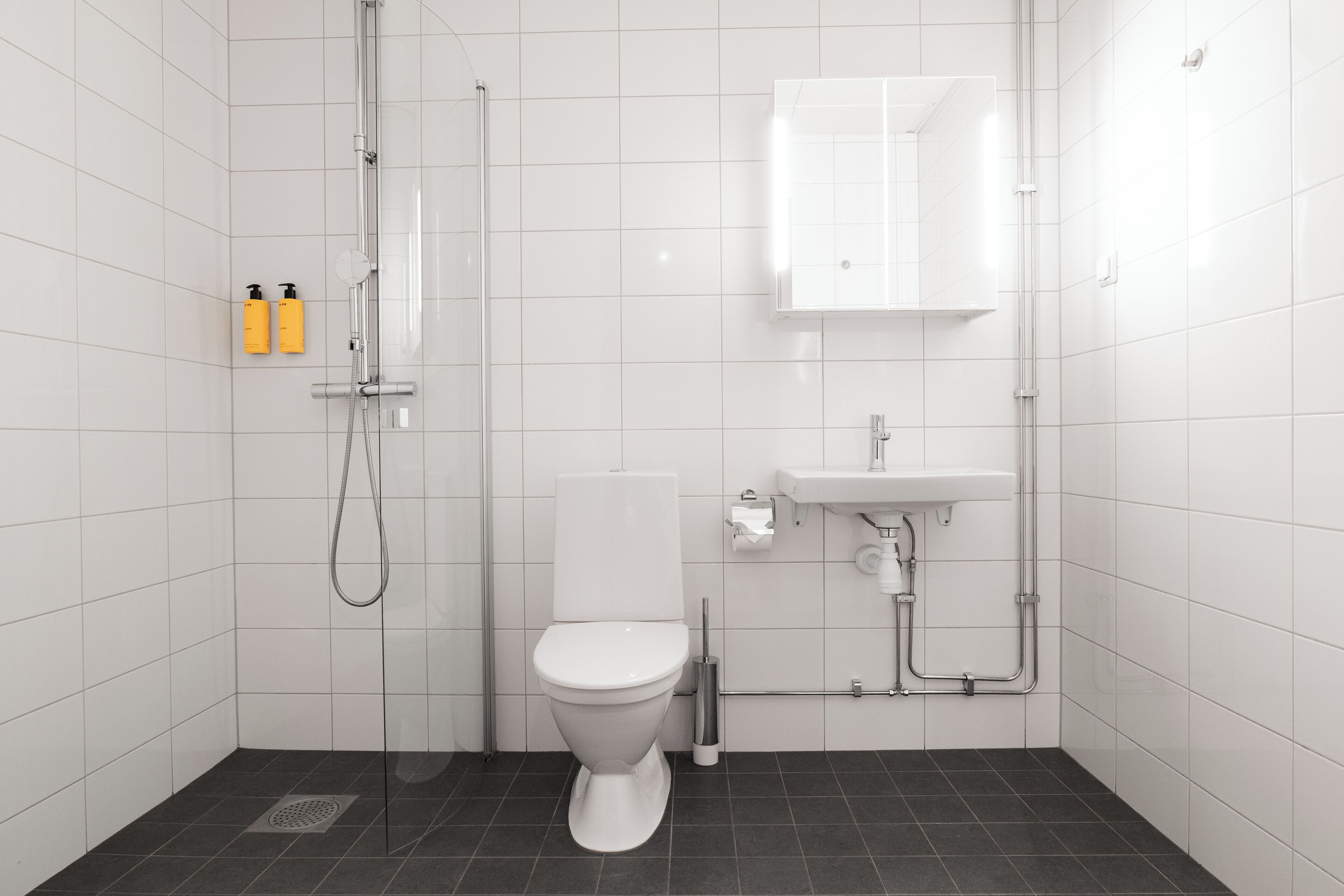 Un baño moderno con azulejos blancos, inodoro, ducha y lavamanos.