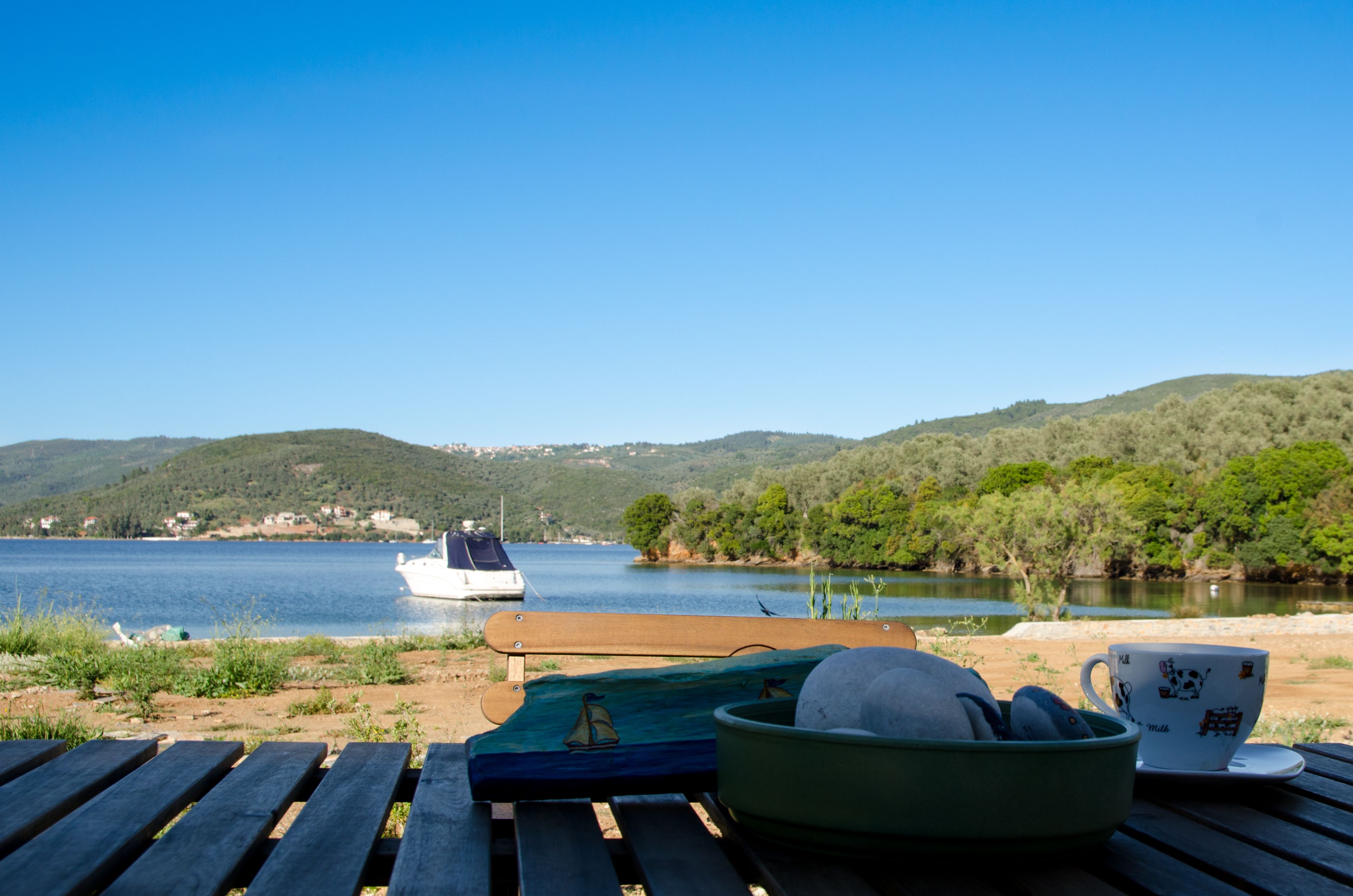 Vista al lago con un bote, una mesa con una taza y un bol, y un banco.