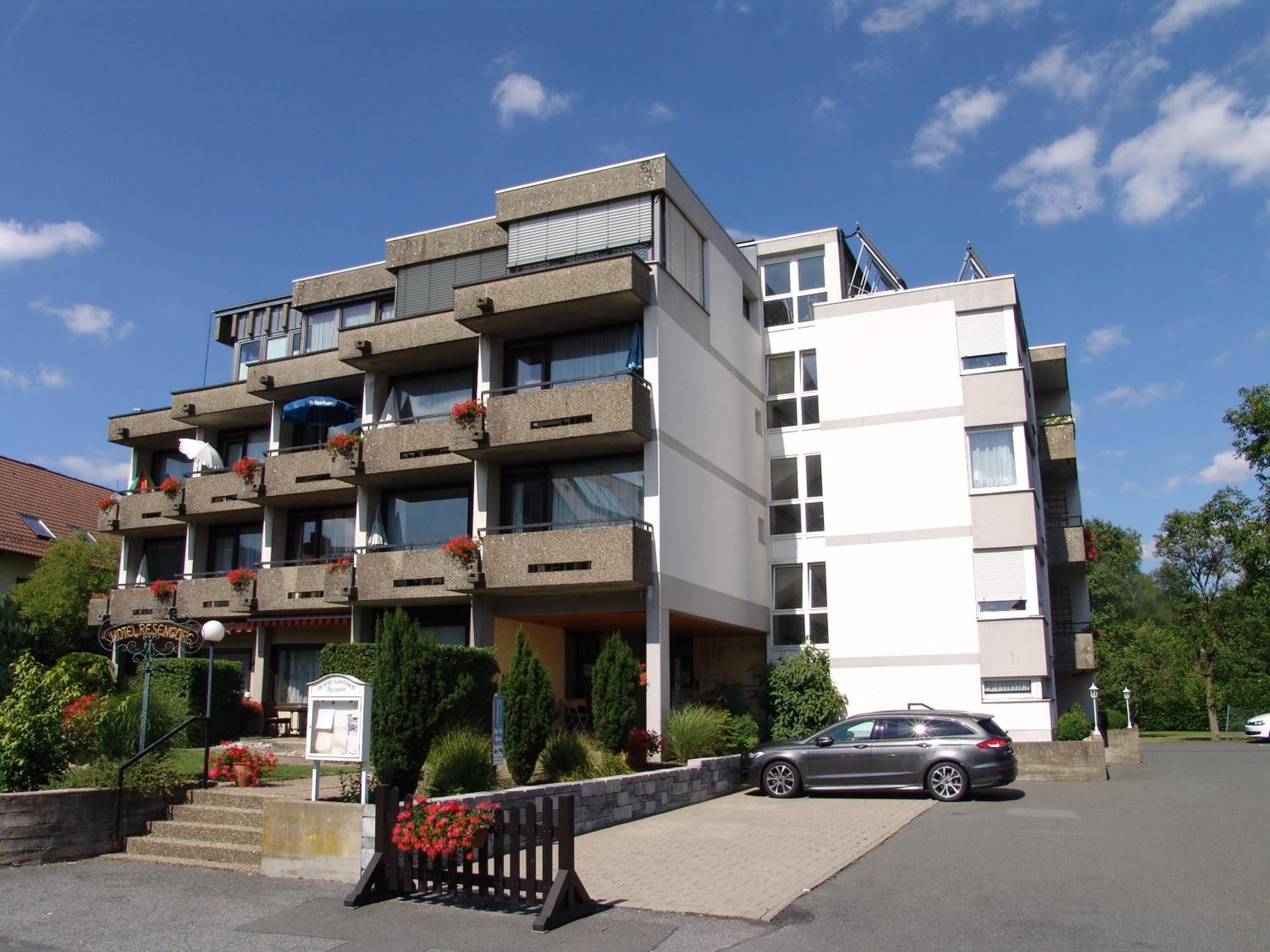 A multi-story hotel with balconies, a parking area, and a sign indicating it is a hotel.