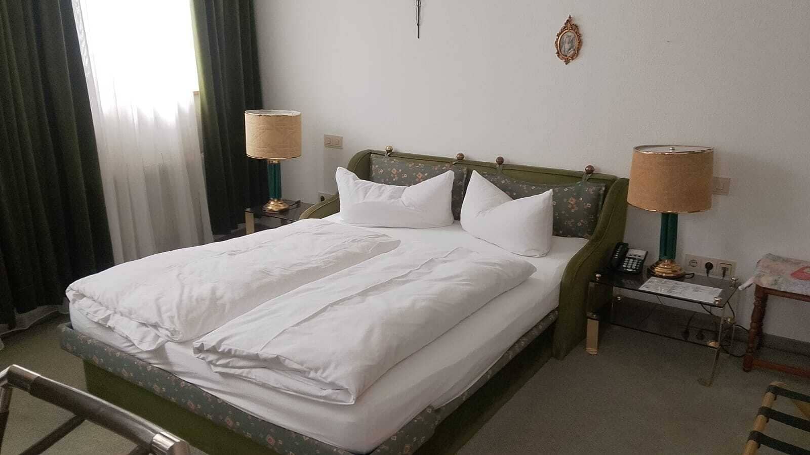 A neatly made bed with white linens, two bedside lamps, a telephone, and a small table with a lamp.
