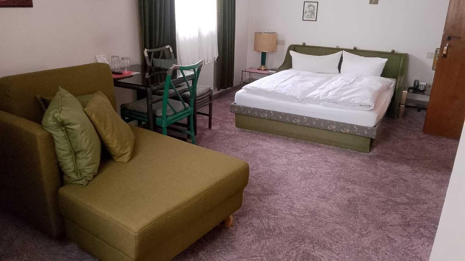 Ein Hotelzimmer mit einem Bett, einem grünen Sofa, einem Esstisch mit Stühlen und einem kleinen Tisch mit einer Lampe.