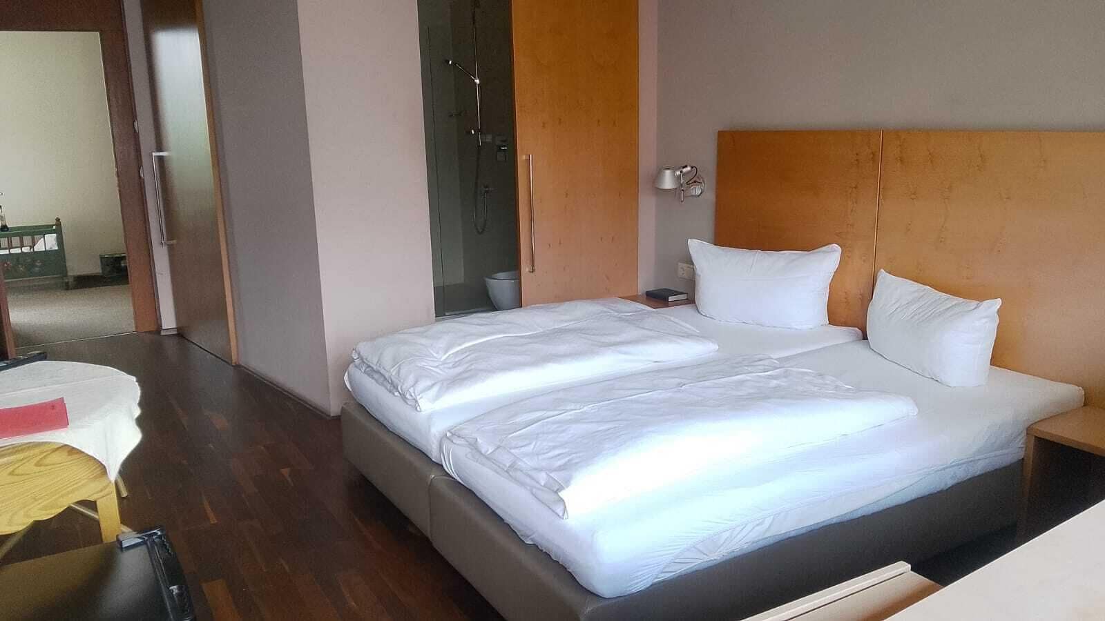 A hotel room with a large bed, a bedside table, a nightstand, and a shower area.