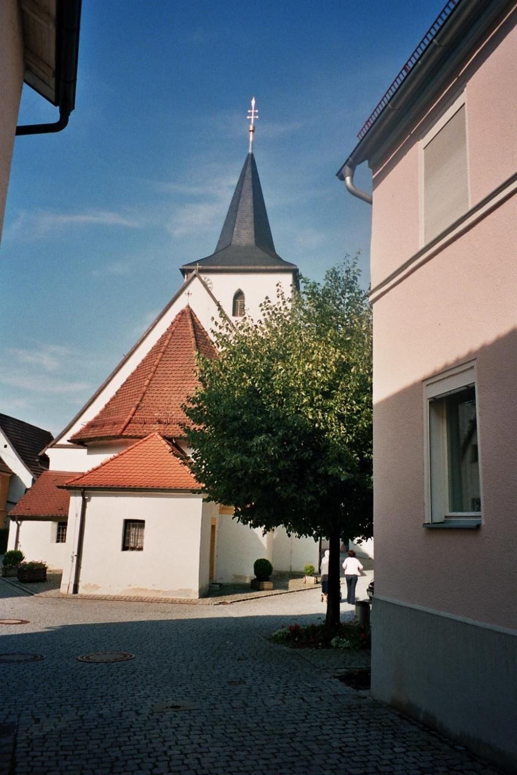 A cobblestone street leading to a church with a tall steeple and a cross on top.