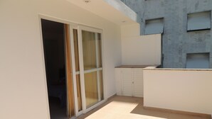 A balcony with a sliding glass door, a tiled floor, and a building with multiple windows in the background. - Ótimo Flat 3 Quartos Vista Cristo Redentor (Rio de Janeiro)