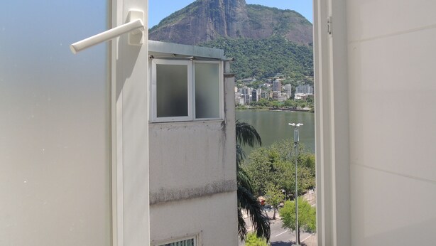 A view from a window overlooking a cityscape with a prominent mountain and a body of water. - Ótimo Flat 3 Quartos Vista Cristo Redentor (Rio de Janeiro)
