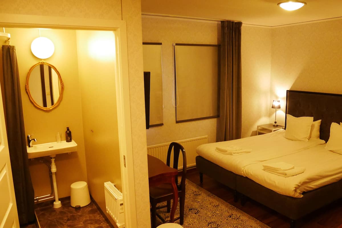A hotel room with a bed, a bedside table with a lamp, a round mirror, a sink, and a chair.
