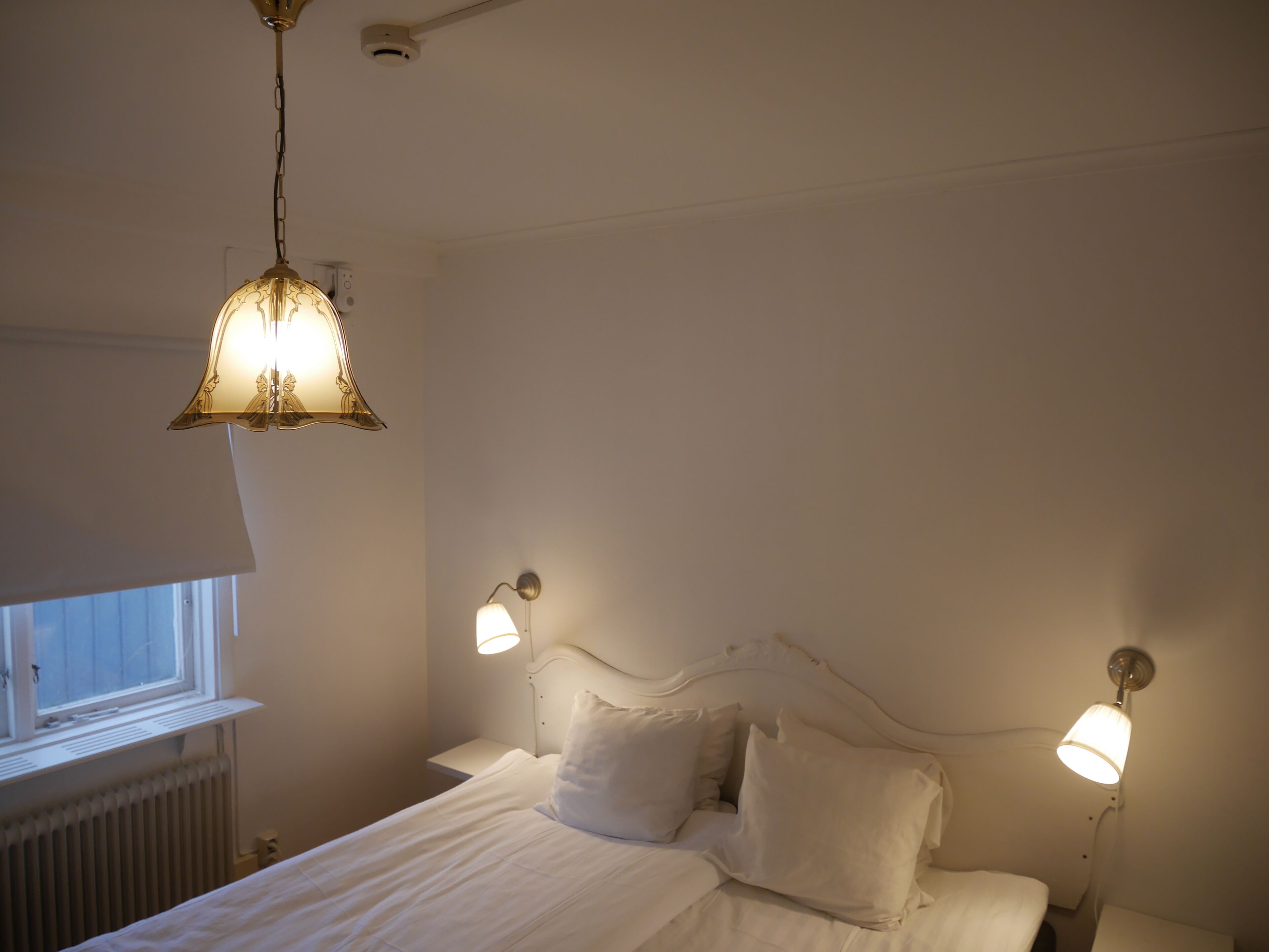 Une chambre à coucher avec un lit, deux lampes de chevet, un luminaire suspendu et une fenêtre.