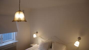 Un dormitorio con cama, dos lámparas de noche, una lámpara colgante y un ventanal.