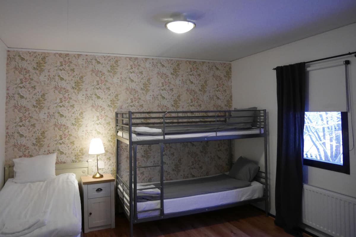 A bunk bed room with a single bed, a nightstand, a lamp, and a window with curtains.