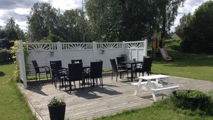 Un patio con valla blanca, sillas negras, una mesa y una mesa de picnic.