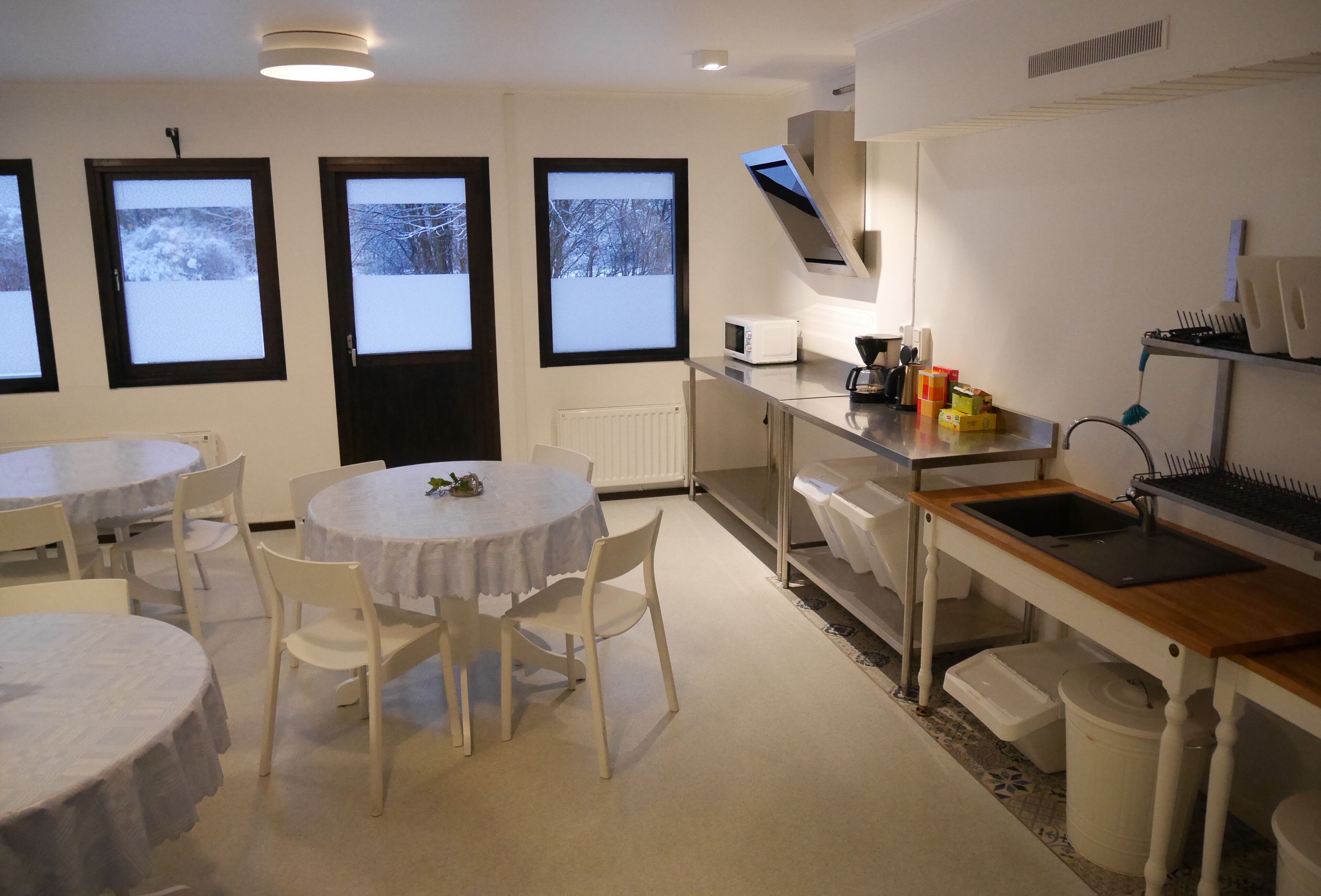 Una cocina moderna con electrodomésticos blancos, un comedor con mesas y sillas redondas, y ventanas amplias con vistas nevadas.