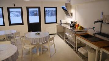 Una cocina moderna con electrodomésticos blancos, un comedor con mesas y sillas redondas, y ventanas amplias con vistas nevadas.