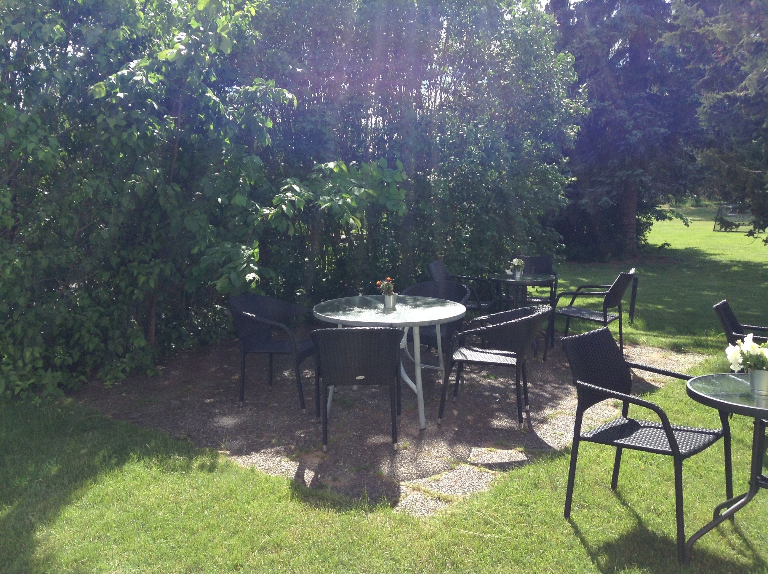 Een terras buiten met een ronde tafel en stoelen, omringd door weelderige beplanting.