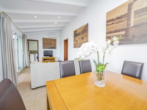 A modern living room with a dining table, chairs, and a vase of white orchids.