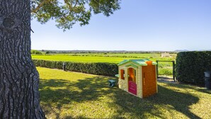 Un arbre, une petite maison de jeu et un champ d’herbe avec une clôture en arrière-plan.