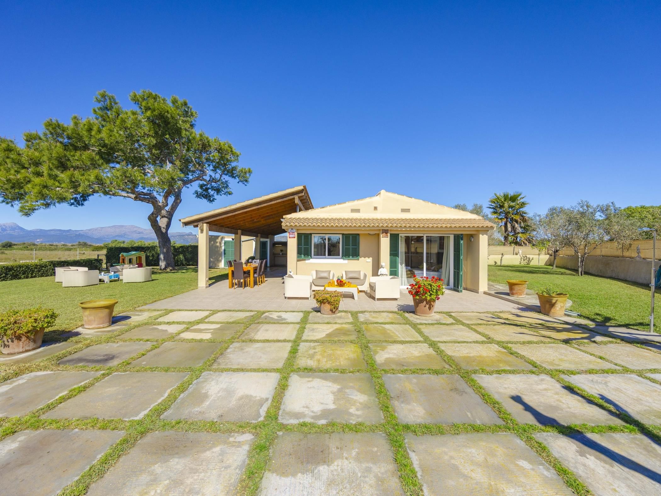 A house with a patio area, outdoor furniture, and a large tree.