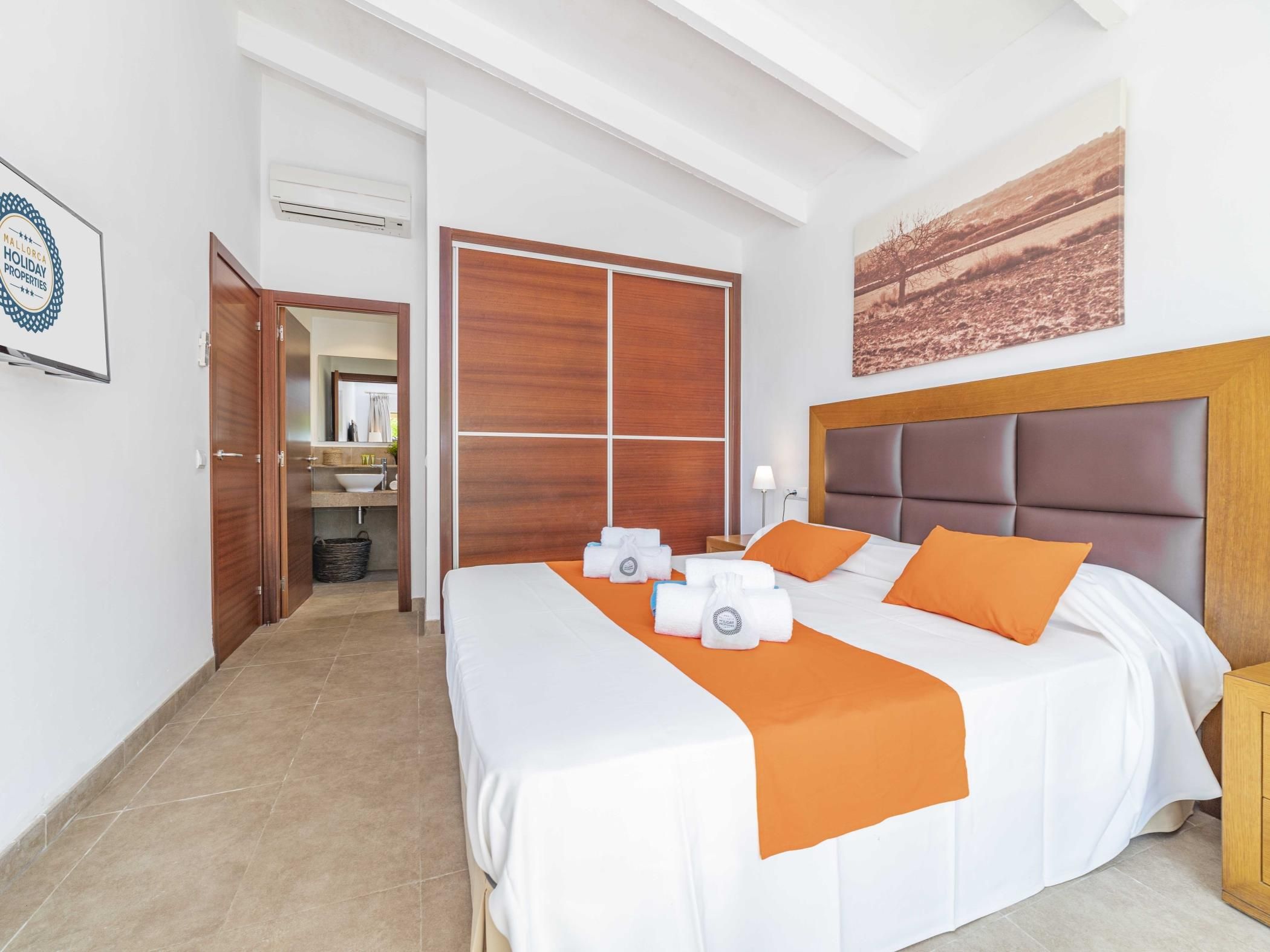 A hotel room with a bed, a nightstand, a bathroom visible through an open door, and a painting on the wall.