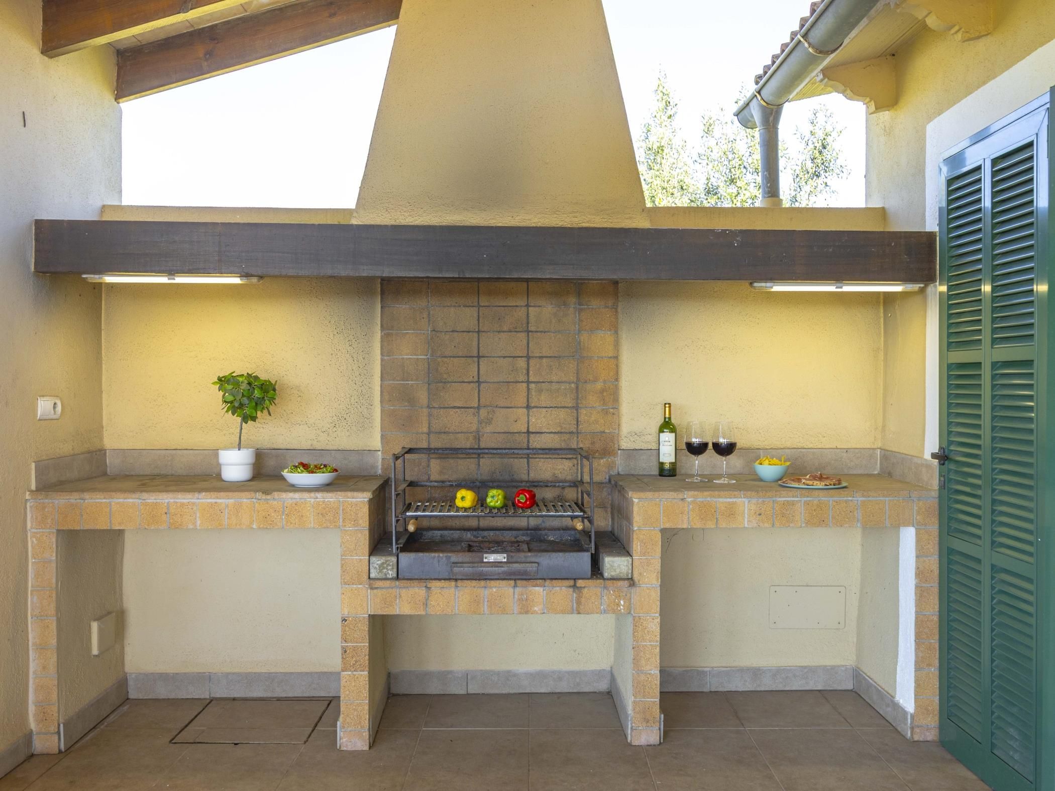 Cocina exterior con una parrilla, dos taburetes de bar, una maceta y una botella de vino.