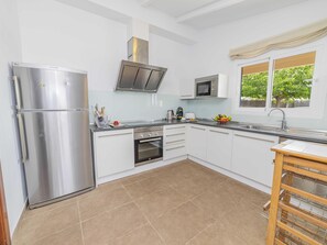 A modern kitchen with a stainless steel refrigerator, built-in oven, microwave, and a window with a view of greenery.